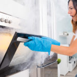 Woman Opening Door Of Oven Full Of Smoke