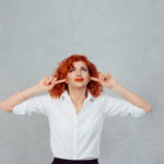 Occlude the ears. Closeup portrait young angry unhappy stressed redhead curly woman covering plugging her ears looking up, stop making loud noise it’s giving me headache isolated gray wall background