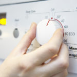 Woman Selecting Cooler Temperature On Washing Machine To Save Energy